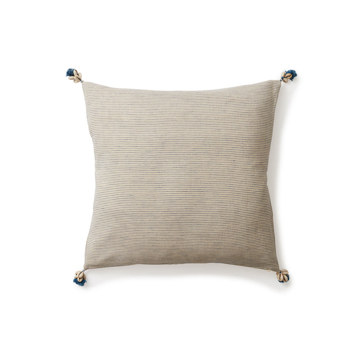 Square throw pillow in a solid woven beige color with navy tassels and tiny clusters of shells sewn on each corner.