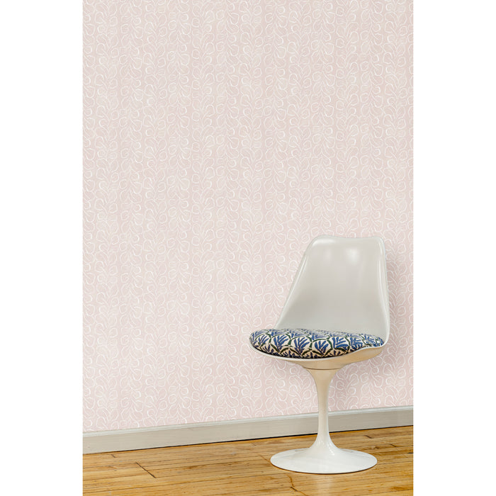 A white swivel chair in front of a wall papered in a large-scale repeating leaf print in white on a light pink watercolor background.