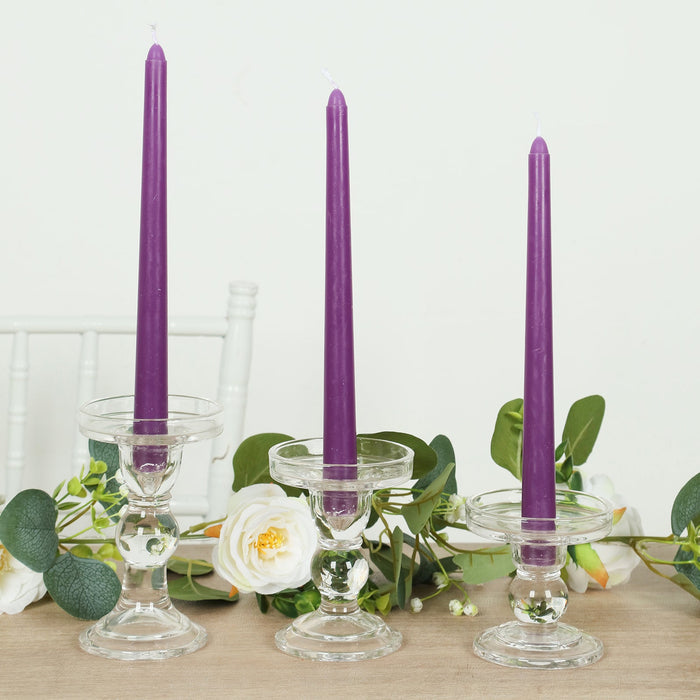 Purple tapered candles in glass holders with greenery decor.