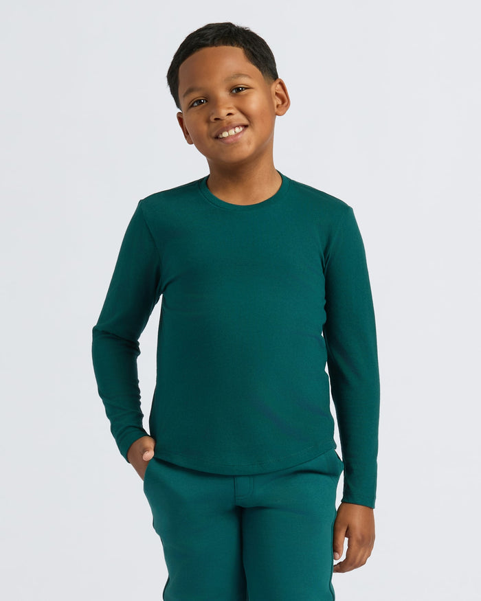 Boy wearing Boys' Classic Long Sleeve Curved Hem Crew Neck, smiling with hands in pockets.