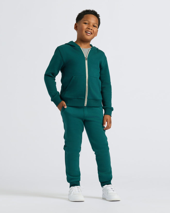 Boy wearing Boys' Deep Emerald Fleece Jogger with a zip-up hoodie, smiling.