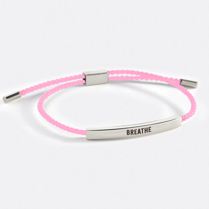 A two-tone inspirational tube bracelet with the word 'BREATHE' printed on it, displayed on a white background with the word 'breathe' also written there.