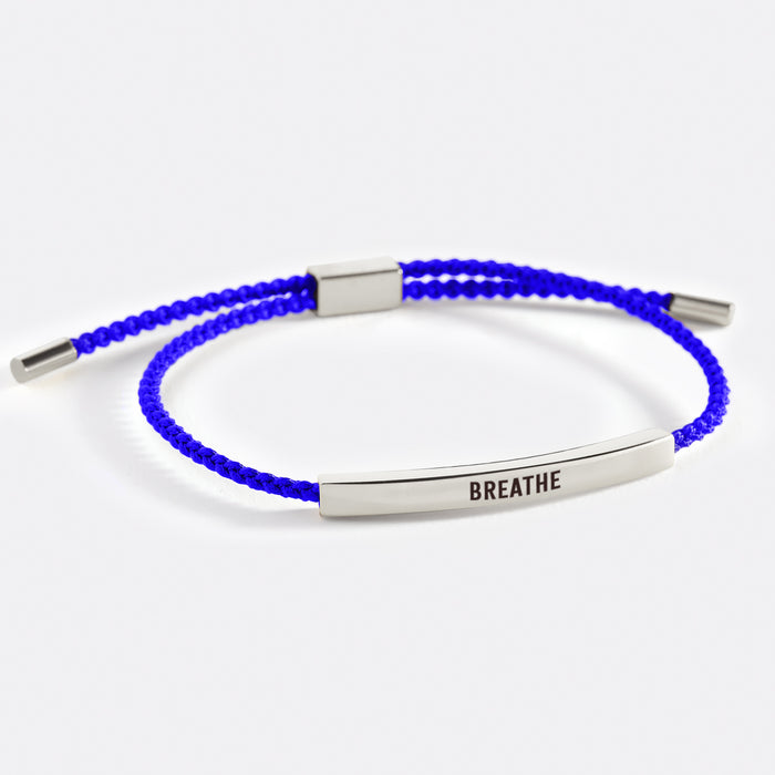 A two-tone inspirational tube bracelet with the word 'BREATHE' printed on it, displayed on a white background with the word 'breathe' also written there.
