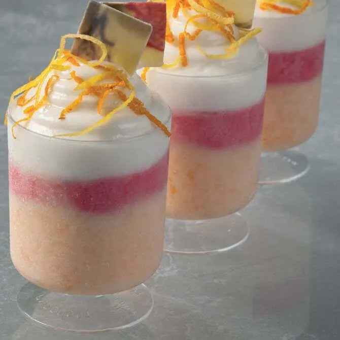 several Cylinder Goblets with Base 5.07 oz Capacity shot filled with orange, pink, and white pastry, garnished with orange peels. Shot on grey foreground.
