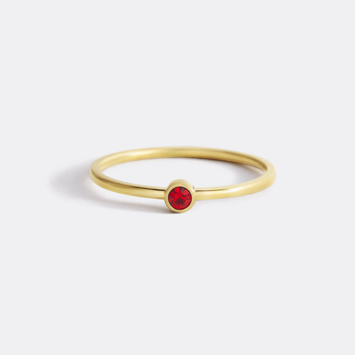 A gold-colored band ring with a bezel-set red birthstone.