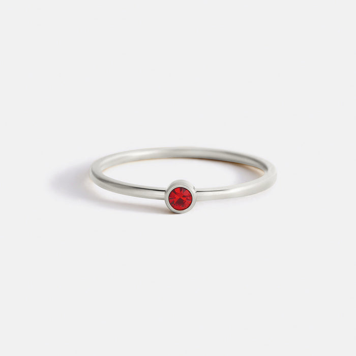 A single gold band ring with a bezel setting containing a red birthstone.