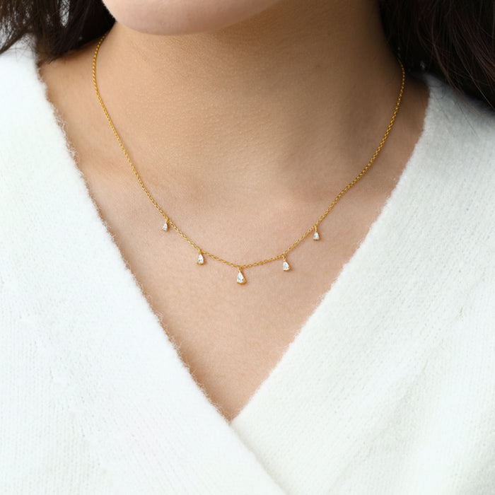 Gold necklace with small pearls worn by a person against a white background