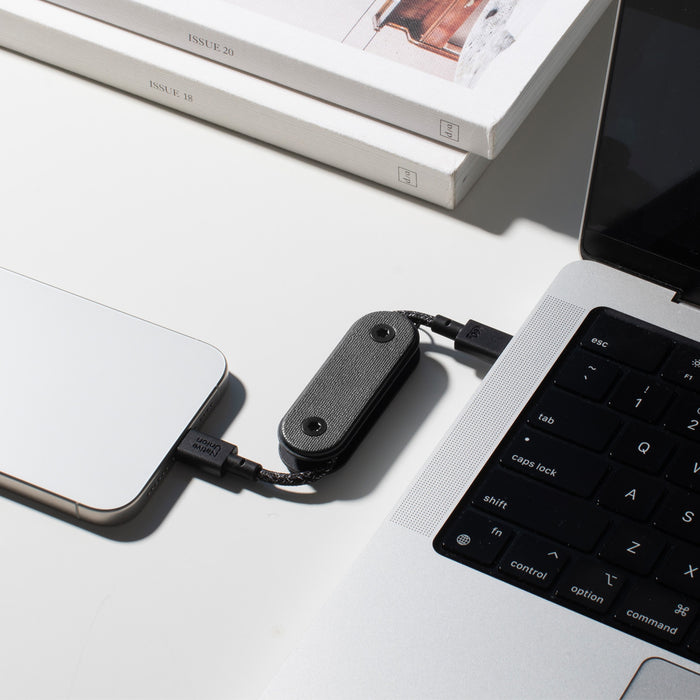 Small black device connected to a laptop and phone on a light surface