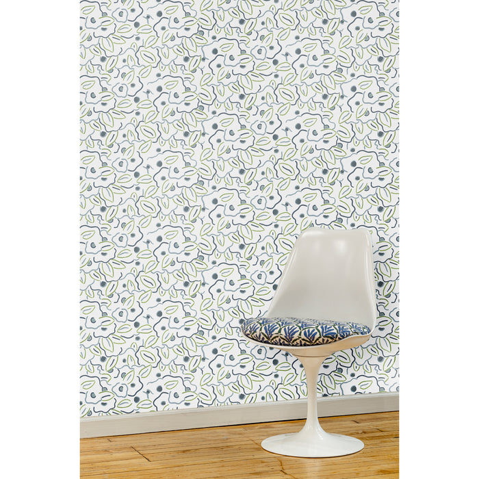 A white swivel chair in front of a wall papered in a large-scale minimal floral print in shades of navy, blue-gray and green on a white background.