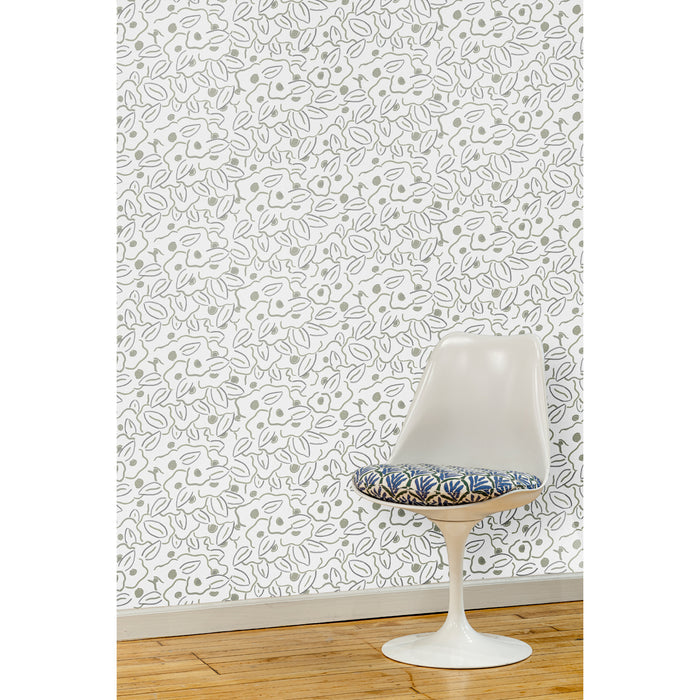 A white swivel chair in front of a wall papered in a large-scale minimal floral print in shades of tan and gray on a white background.