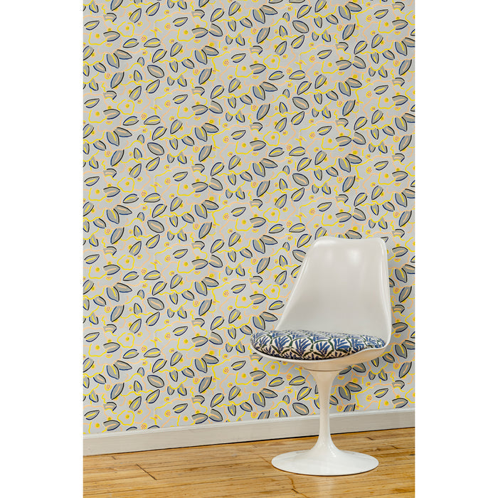 A white swivel chair in front of a wall papered in a large-scale minimal floral print in shades of navy, yellow and pink on a gray-blue background.